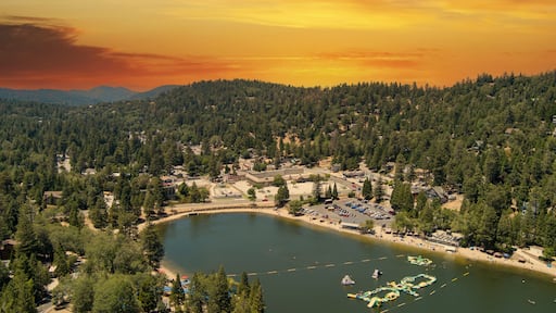 aerial shot of a gorgeous summer landscape with rippling lake water, lush green trees, grass and plants with homes on the hillside, powerful clouds at sunset at Lake Gregory in Crestline California