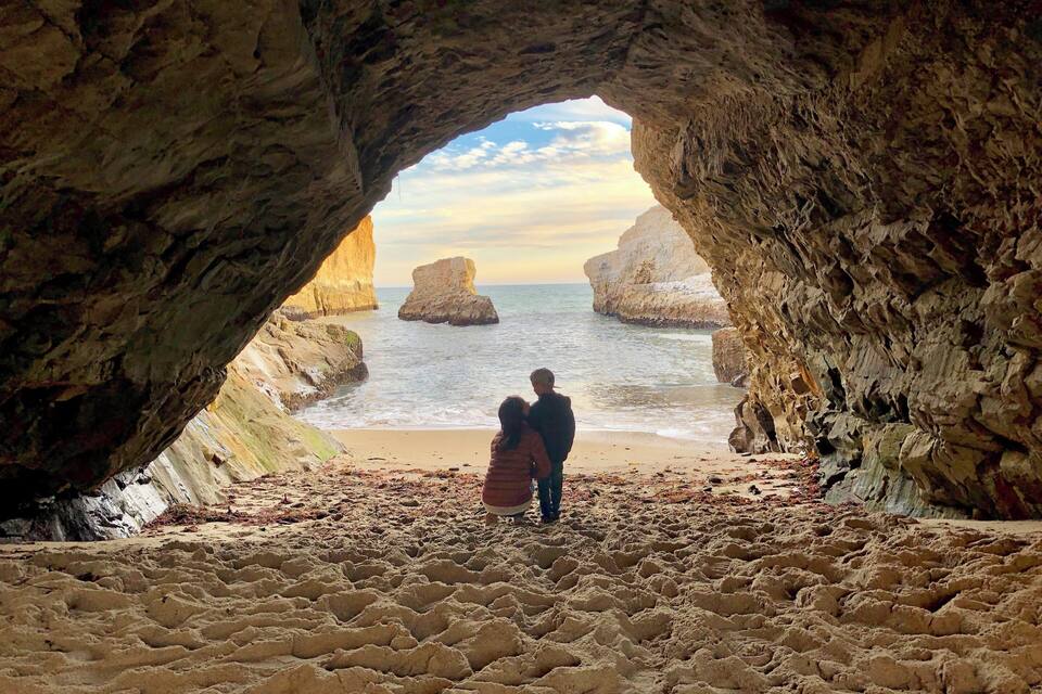 A cave opening to a beach with two people standing in the middle.