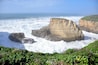A coastal landscape with rocky cliffs and waves crashing against them.