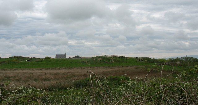 Un campo cubierto de hierba con un edificio pequeño a lo lejos bajo un cielo nublado.
