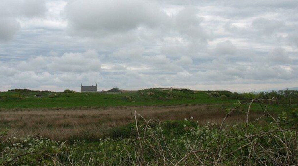 Un campo cubierto de hierba con un edificio pequeño a lo lejos bajo un cielo nublado.