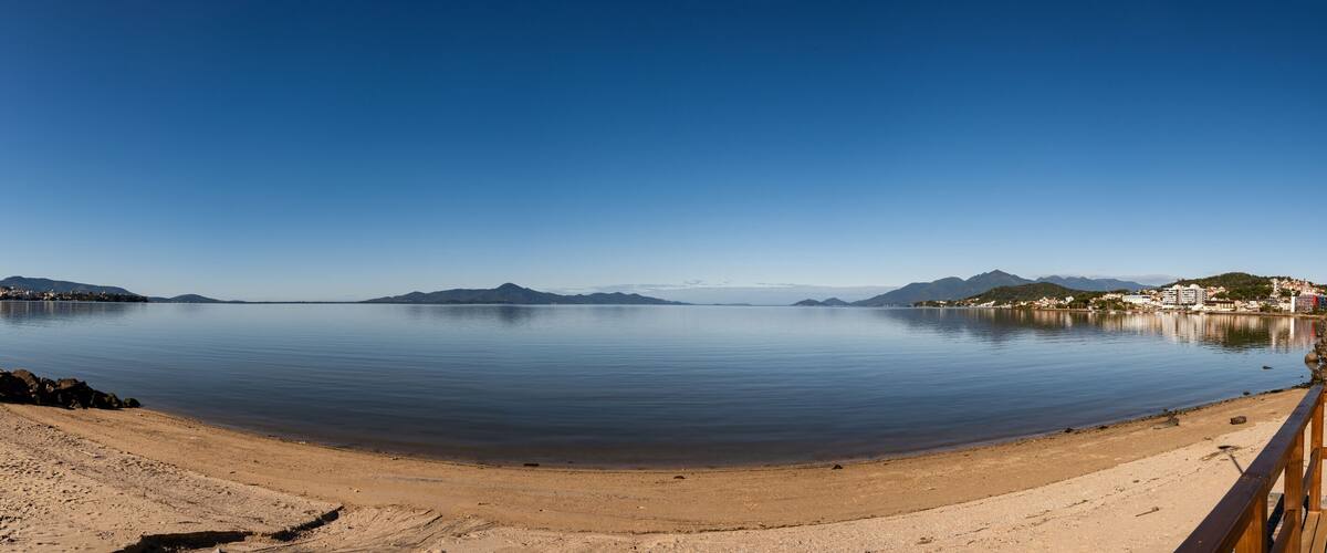 A calm beach with a wooden walkway, clear blue sky, and distant mountains.