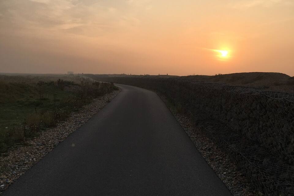 Une route de campagne sinueuse traverse un champ, avec un coucher de soleil en arrière-plan.