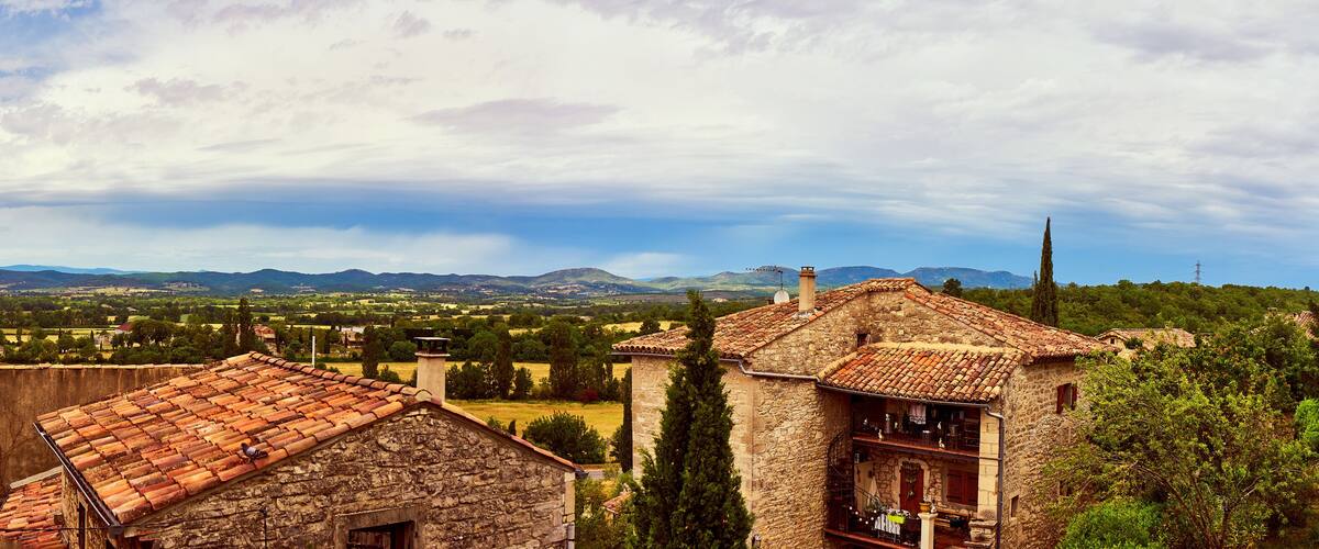 A stone building with a tiled roof overlooking a valley with mountains in the background.
