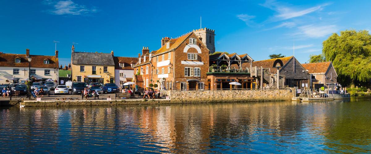 A riverside town with historic buildings, a stone bridge, and boats docked along the water.