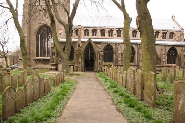 A church with a central aisle flanked by tombstones, surrounded by trees.