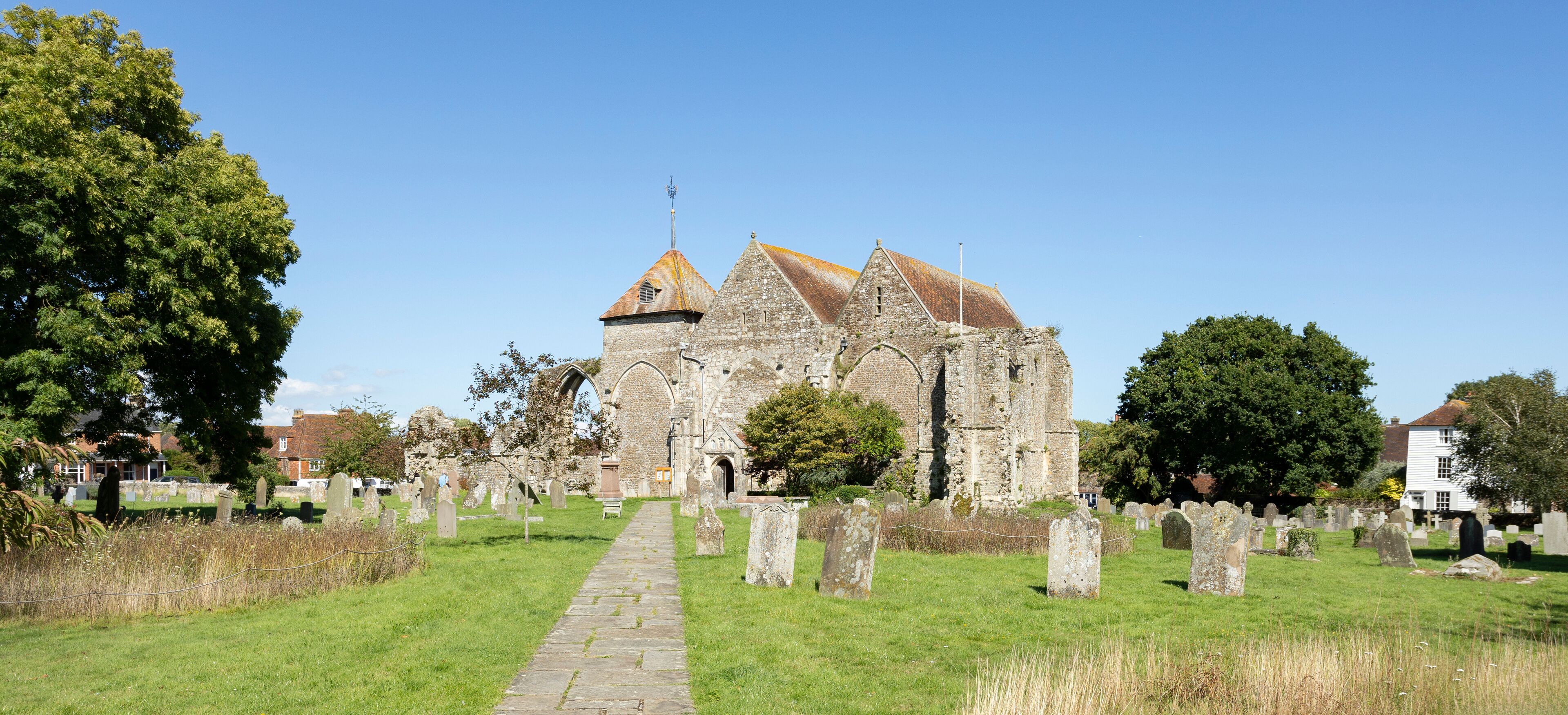 A historic church with a stone pathway leading to its entrance, surrounded by a cemetery with numerous headstones.