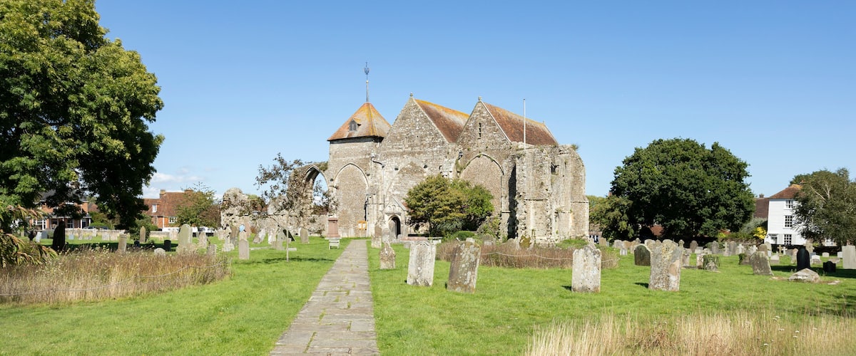 A historic church with a stone pathway leading to its entrance, surrounded by a cemetery with numerous headstones.