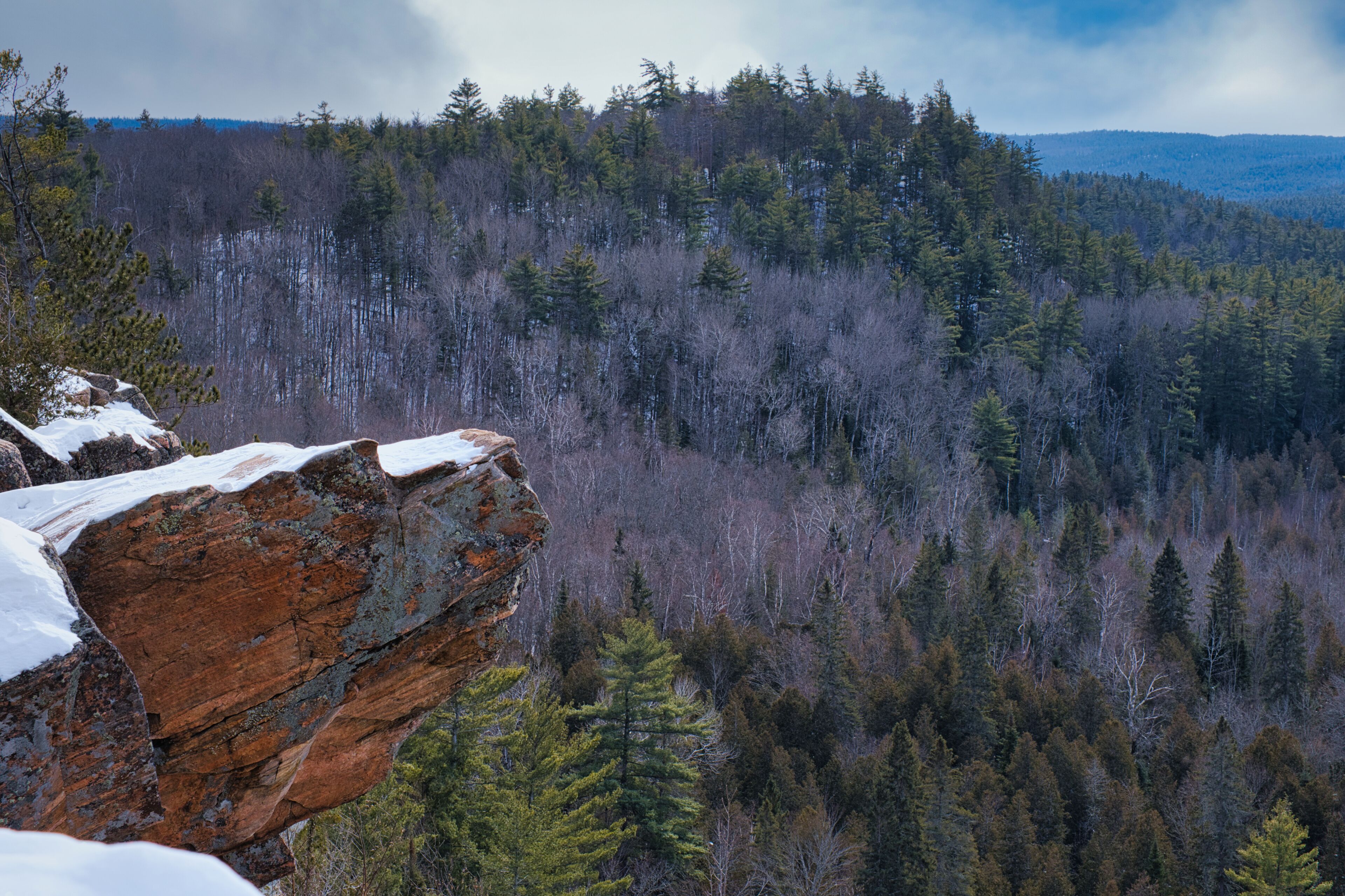 A forested mountain landscape with a prominent rock formation in the foreground.