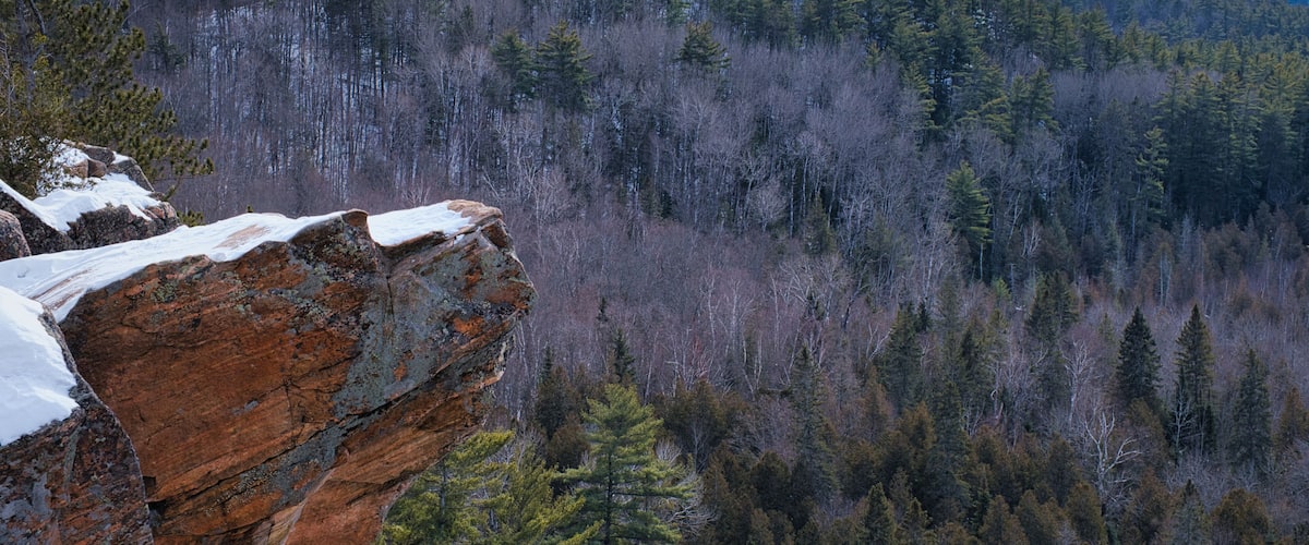 A forested mountain landscape with a prominent rock formation in the foreground.