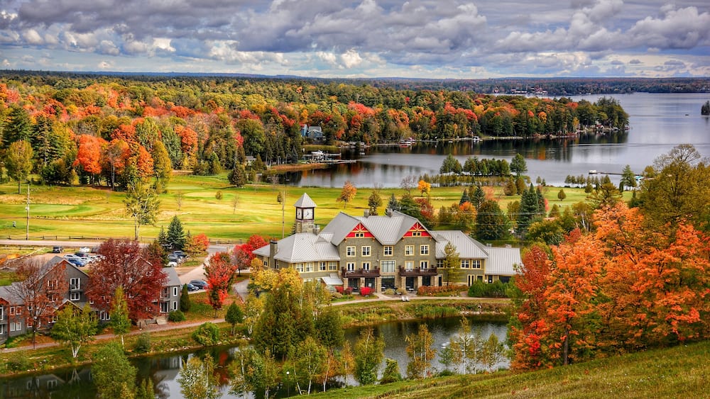 A lakeside resort with autumn foliage, a golf course, and a prominent building with a clock tower.