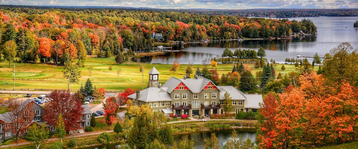 A lakeside resort with autumn foliage, a golf course, and a prominent building with a clock tower.