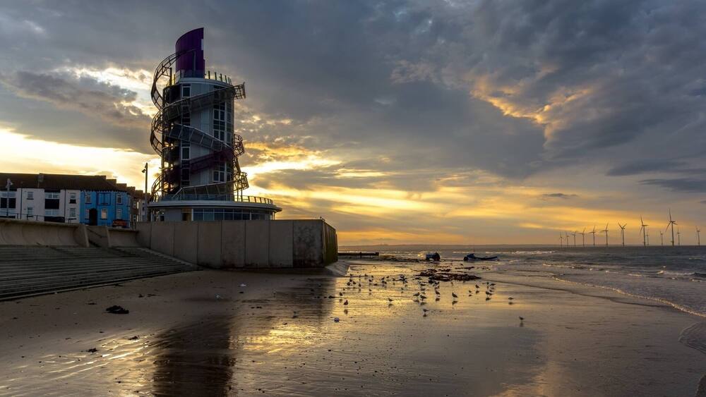 Un paysage côtier avec une éolienne, une jetée et un coucher de soleil.