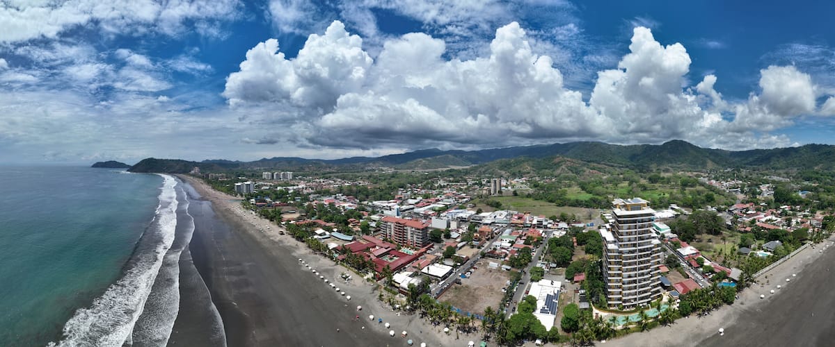 A coastal city with a beach, buildings, and mountains in the background.