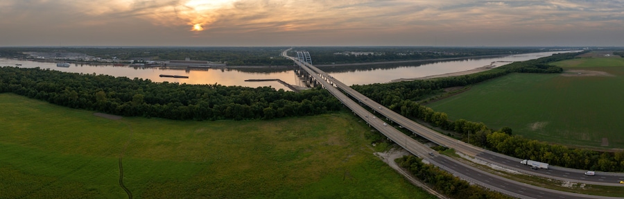 A bridge over a river with surrounding greenery and industrial buildings.