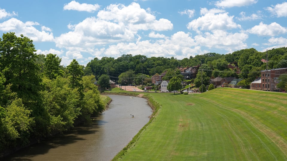 A river flowing through a green landscape with houses and trees in the background.