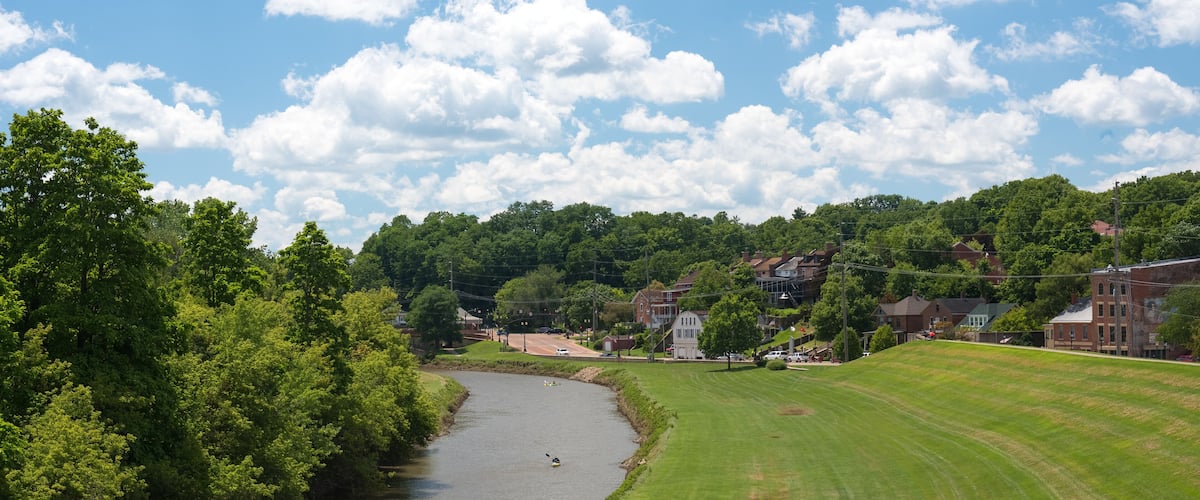 A river flowing through a green landscape with houses and trees in the background.