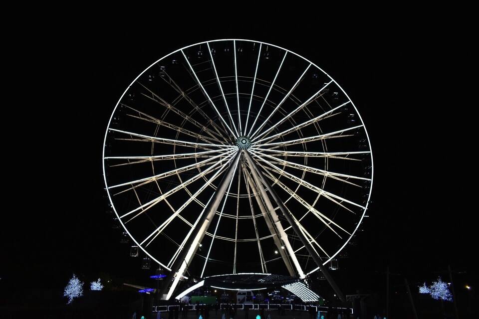 A large Ferris wheel at night with illuminated spokes and a dark sky background.