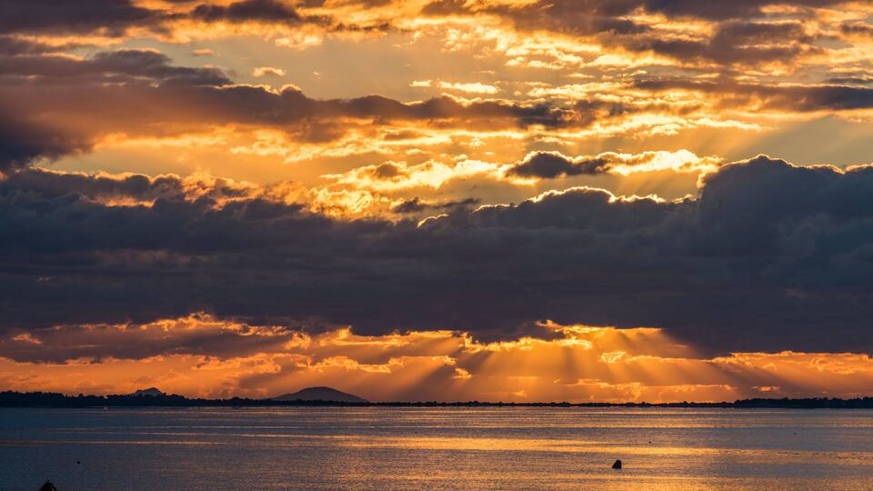 A sunset over a body of water with clouds reflecting golden light.