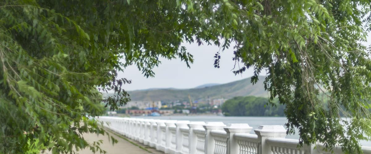 A paved walkway with white balustrades, a river, and a distant town.