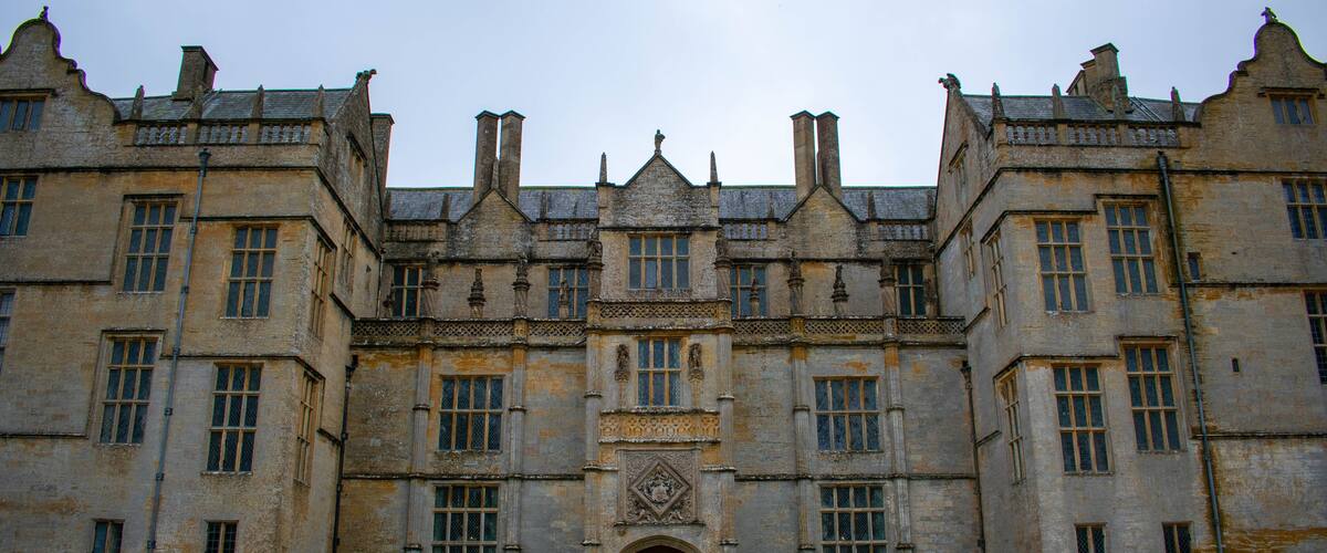 A large, historic building with symmetrical architecture, a central entrance, and well-maintained green lawns.