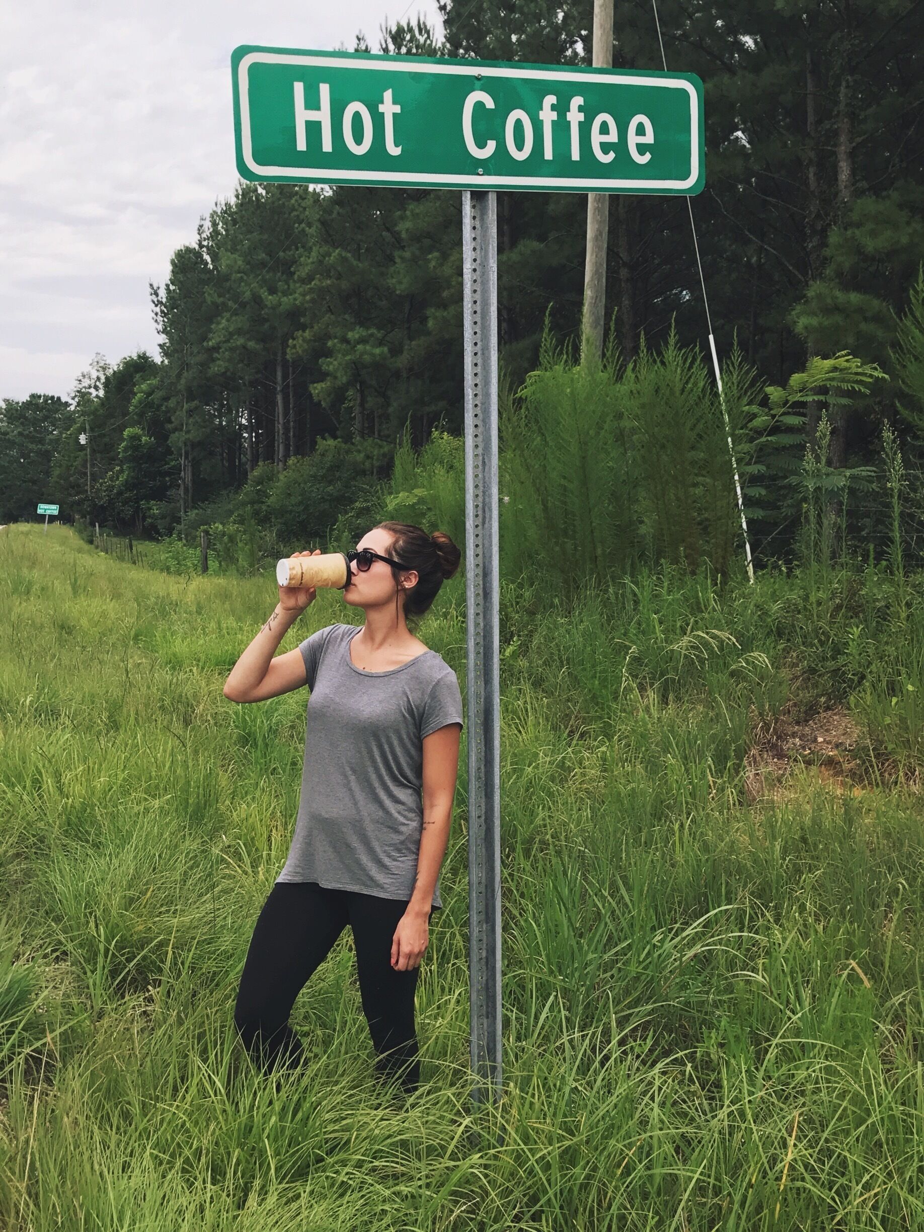 A person drinking from a cup near a sign that reads "Hot Coffee."