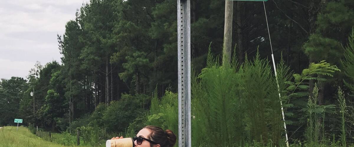 A person drinking from a cup near a sign that reads "Hot Coffee."