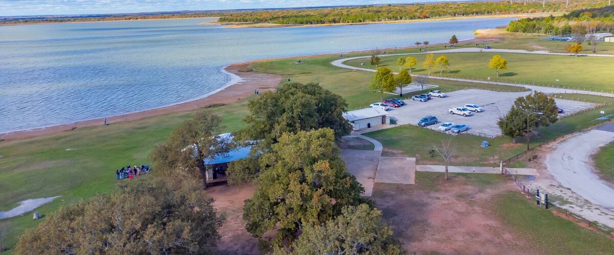 A lakeside park with a parking area, picnic tables, and a gazebo.