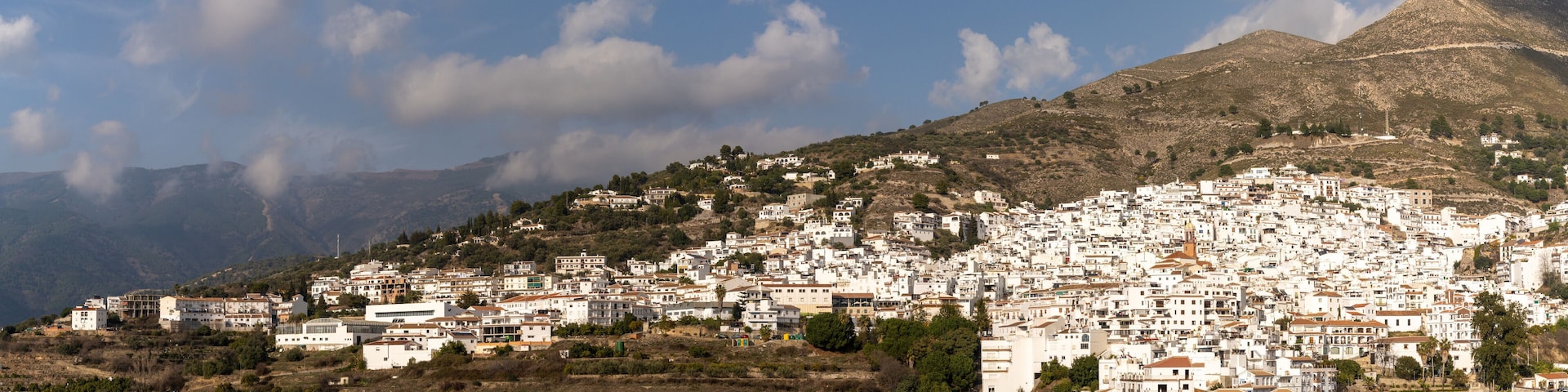 A densely packed hillside town with white buildings, surrounded by mountains and a clear sky.