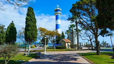 Un faro, un parque con bancos y un cielo azul despejado.
