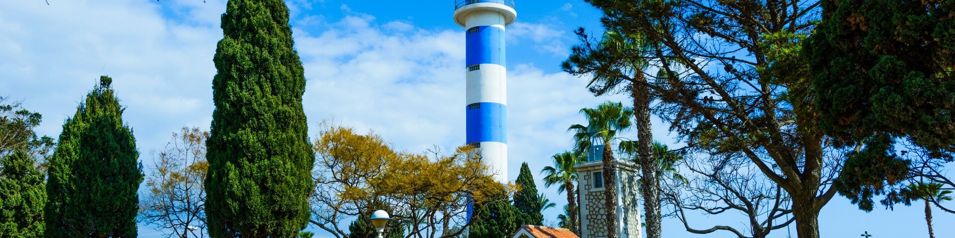 Un faro, un parque con bancos y un cielo azul despejado.