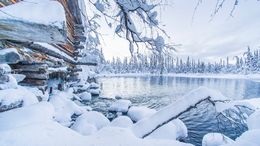 A log cabin surrounded by snow-covered trees and a frozen lake.