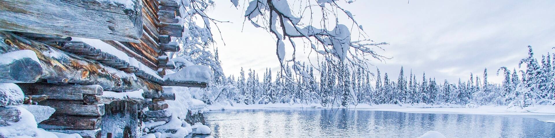 A log cabin surrounded by snow-covered trees and a frozen lake.