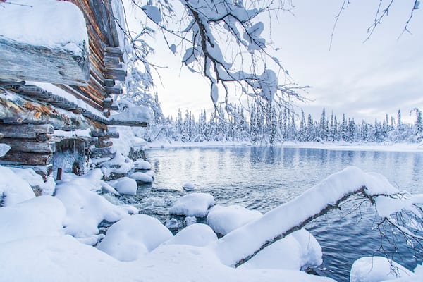 A log cabin surrounded by snow-covered trees and a frozen lake.