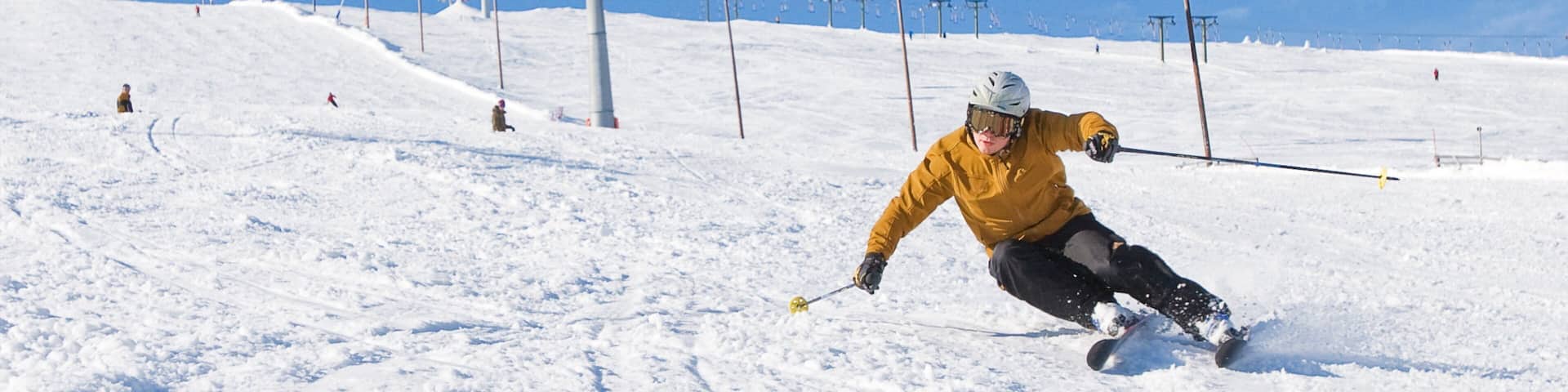 A skier skiing down a snowy slope with ski lifts in the background.