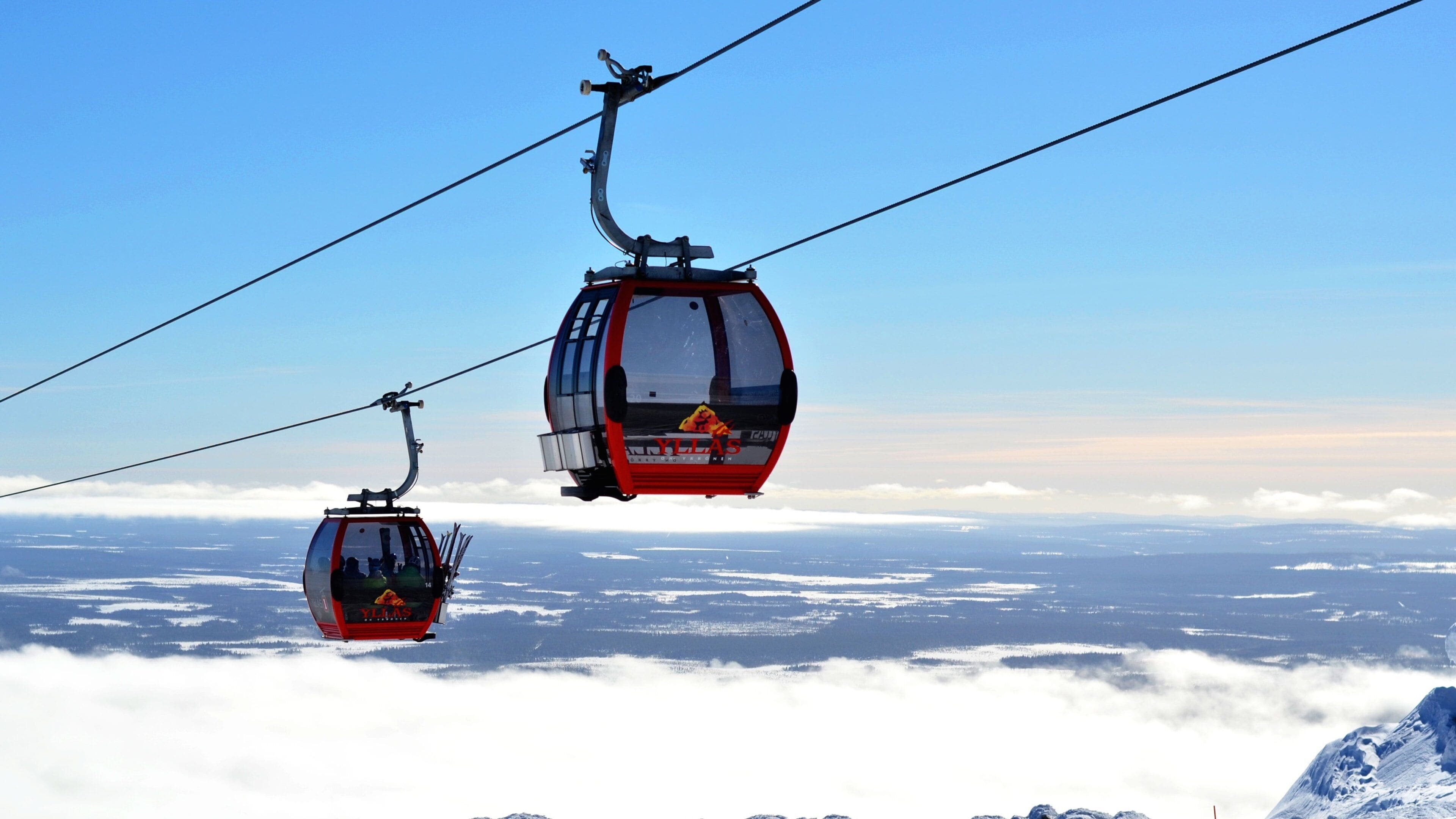 Two red cable cars with the logo "YLLAS" flying over a snowy landscape.