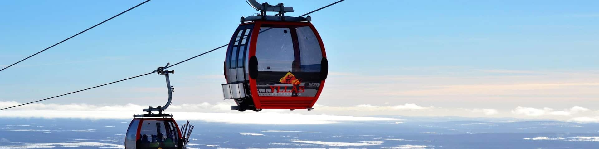 Two red cable cars with the logo "YLLAS" flying over a snowy landscape.