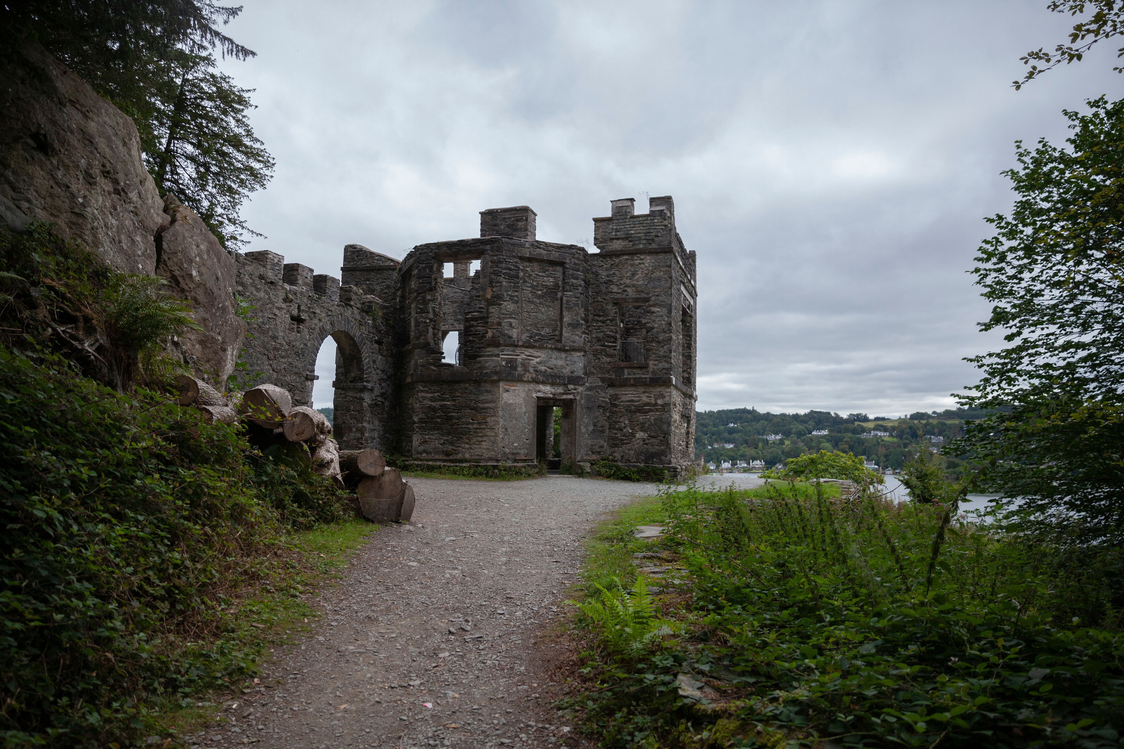 A historic stone castle ruin with a gravel path leading to it, surrounded by greenery and overlooking a body of water.