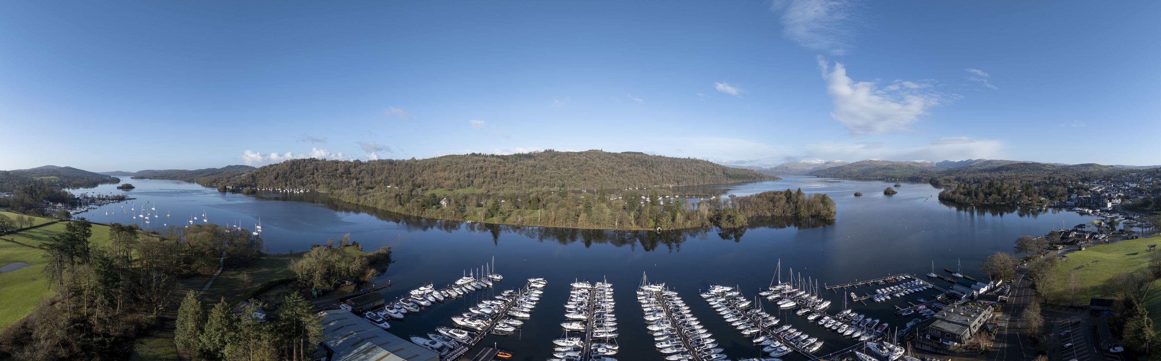 Aerial view of boats nestled in the marina's embrace, reflecting the sky's hue, with the backdrop of the lush fells, Bowness-on-Windermere, England, United Kingdom.
