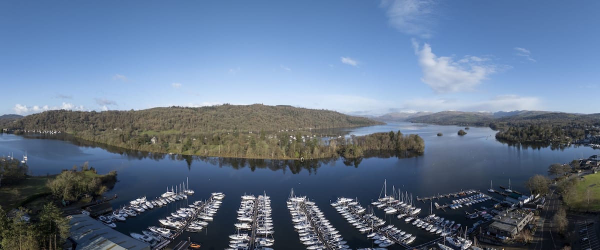 Aerial view of boats nestled in the marina's embrace, reflecting the sky's hue, with the backdrop of the lush fells, Bowness-on-Windermere, England, United Kingdom.