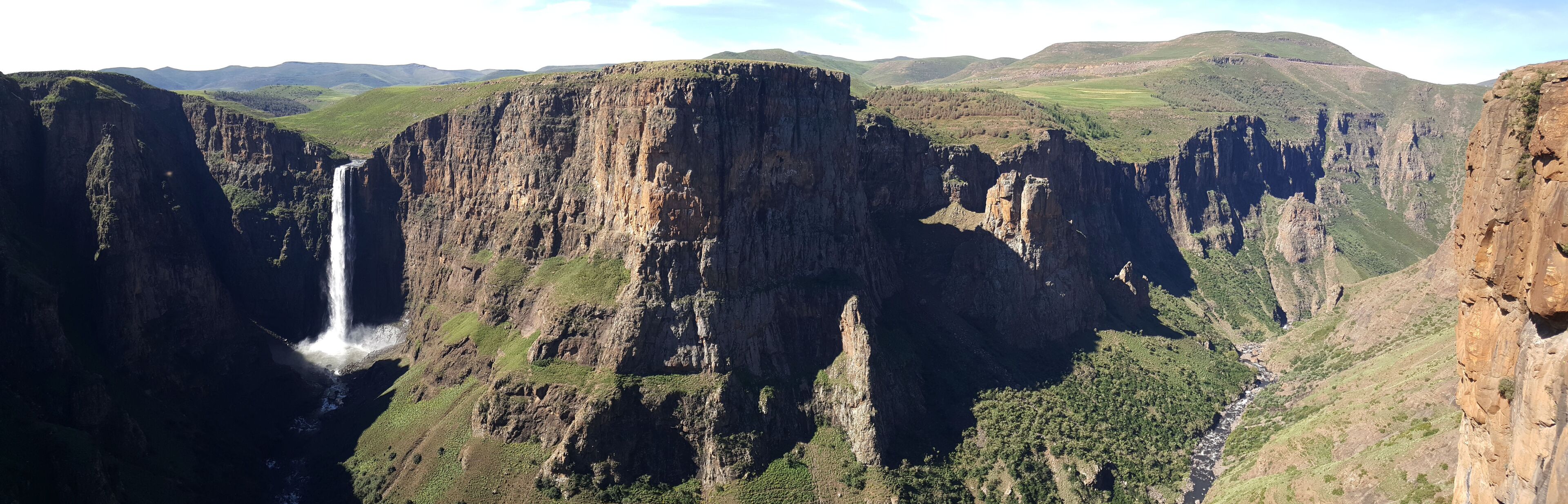 A waterfall cascading down a steep cliff surrounded by lush green hills.
