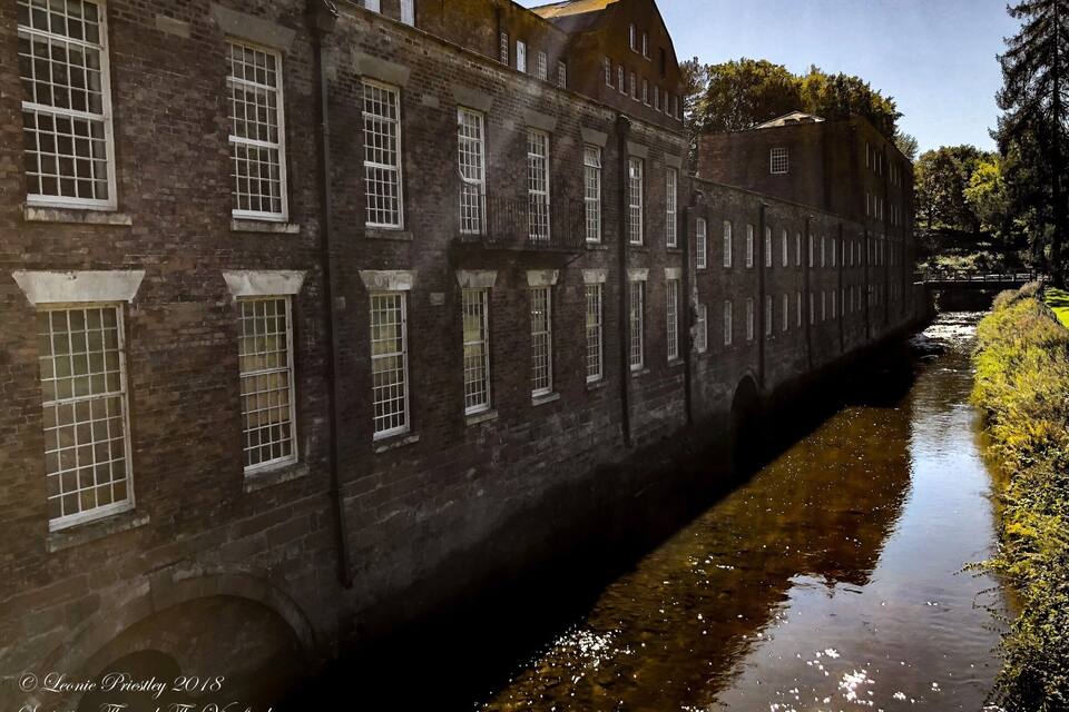 A brick building with large windows and a narrow waterway beside it.