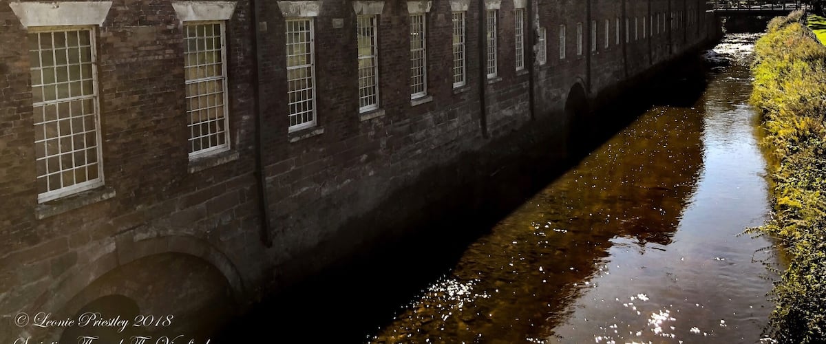 A brick building with large windows and a narrow waterway beside it.