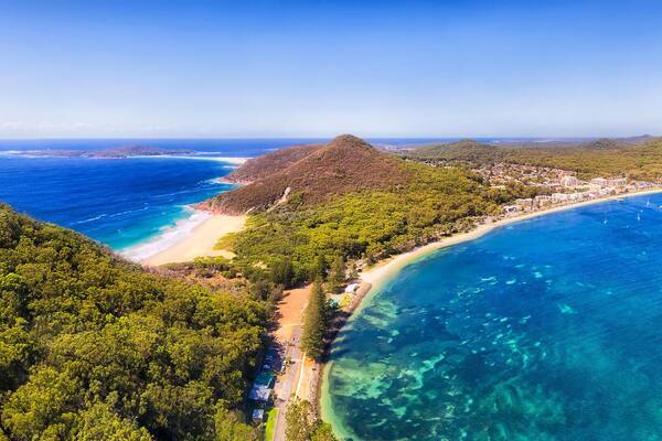 A coastal landscape with a beach, clear blue waters, and lush green hills.