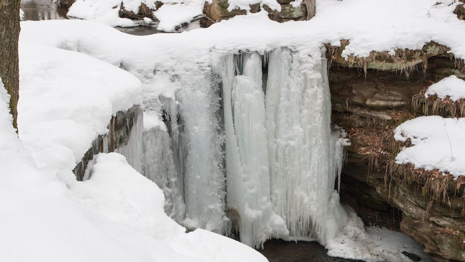 A frozen waterfall with snow-covered rocks and trees.