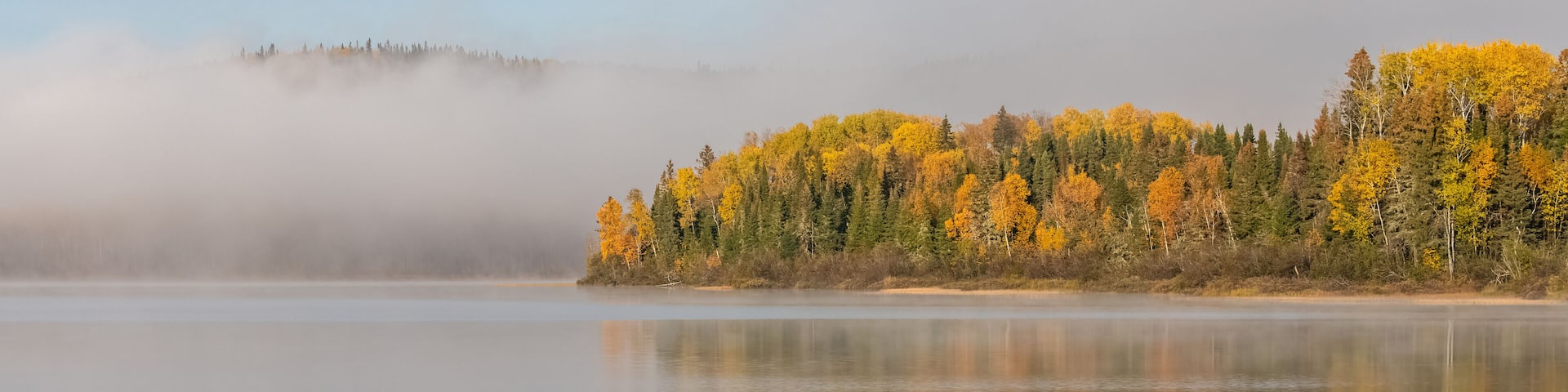 A lake in the forest in Canada, during the Indian summer, with fog on the water in the morning