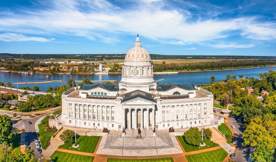 A large government building with a prominent dome, surrounded by a river and green spaces.