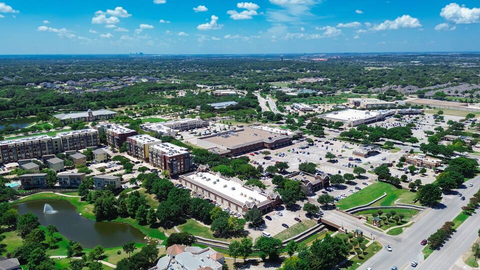 An aerial view of a suburban area with residential buildings, a large parking lot, and a lake.