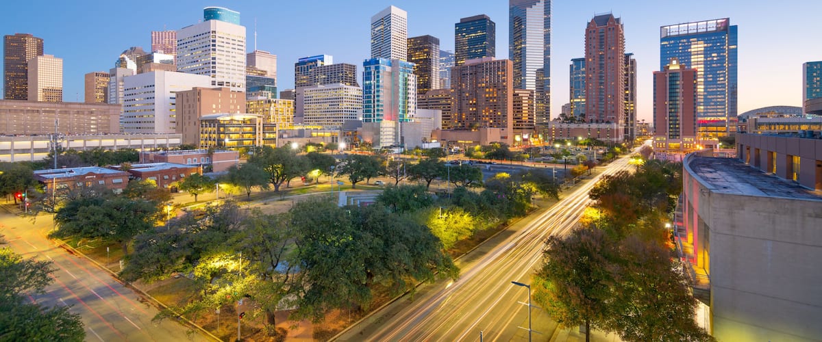 A city skyline with modern high-rise buildings, a river, and a park with trees.