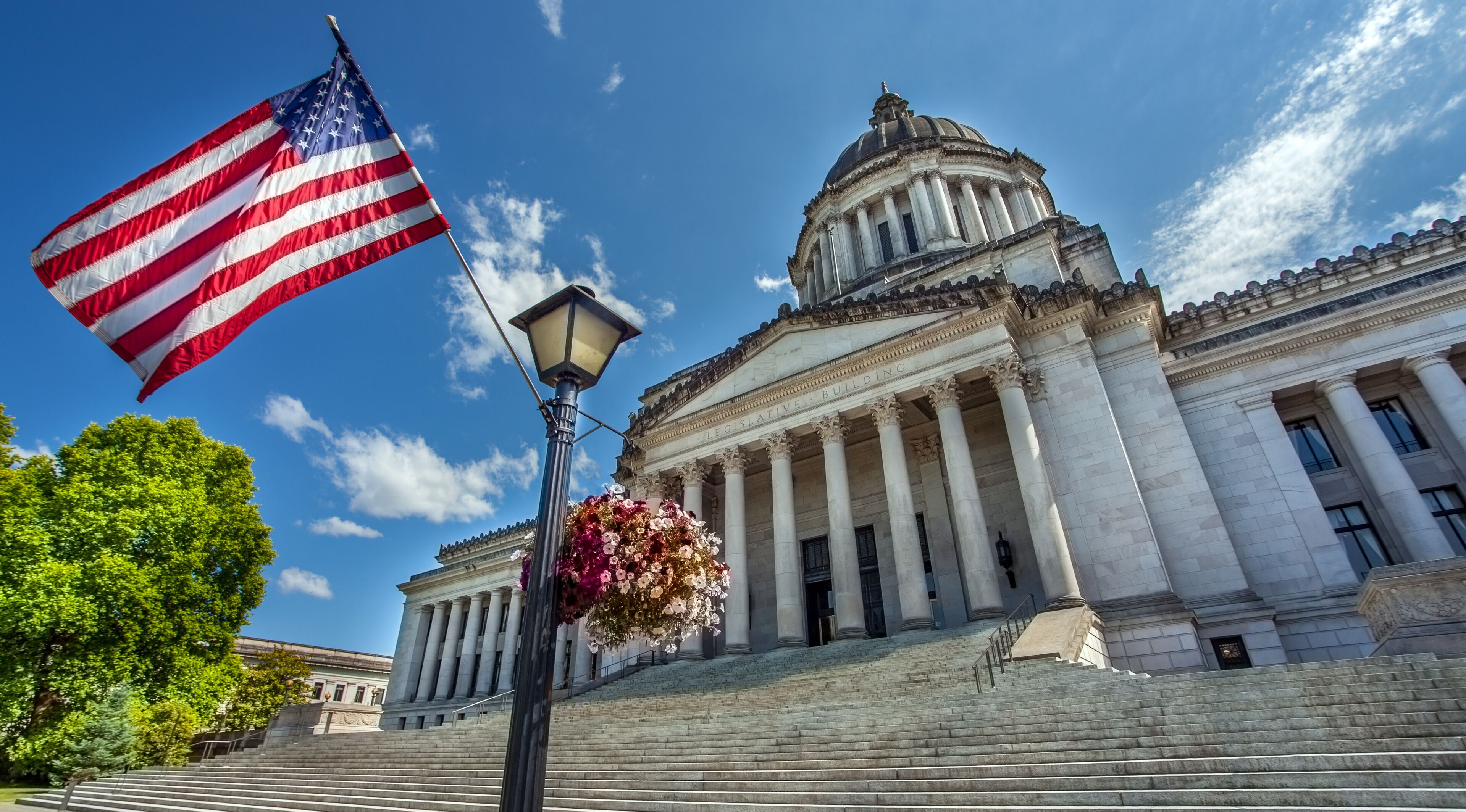 A neoclassical building with a dome and columns, an American flag, and a street lamp with flowers.